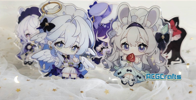 May include: Two anime-style acrylic character stands. The character on the left is wearing a white dress with blue and purple accents, a halo, and angel wings. The character on the right is wearing a white dress with blue and green accents, a white bunny ear headband, and a red apple in her hand. The text "ACGCrafts" is visible in the bottom right corner of the image.