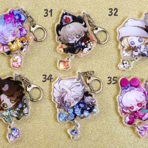 May include: Five colorful character keychains with silver key rings. Each keychain features a different character with a unique design and a small charm hanging below. The characters are a girl with blue hair, a boy with brown hair, a girl with white hair, a boy with white hair, and a girl with pink hair.