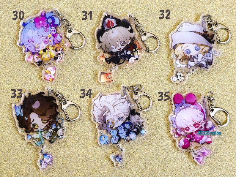 May include: Five colorful character keychains with silver key rings. Each keychain features a different character with a unique design and a small charm hanging below. The characters are a girl with blue hair, a boy with brown hair, a girl with white hair, a boy with white hair, and a girl with pink hair.