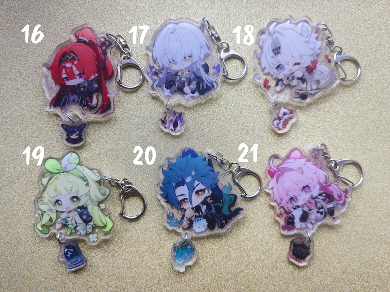 May include: A collection of six anime-style acrylic keychains. Each keychain features a colorful character design with a silver-colored clasp and a small charm. The keychains are numbered 16 through 21.