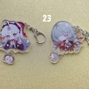 May include: Two anime-style acrylic keychains featuring female characters with large eyes and detailed outfits. One keychain has a white-haired character with pink accents, the other has a gray-haired character with red accents. Both have silver key rings.