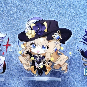 May include: Three anime character acrylic stands. The characters are a white-haired male with red eyes, a blonde female with blue eyes, and a purple-haired male with blue eyes. The stands are on a blue background.