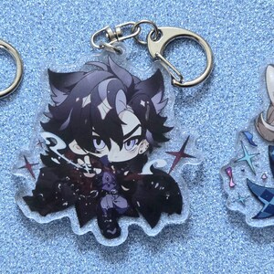 May include: Three anime-style character keychains with glitter accents. The characters are a white-haired male with purple eyes, a black-haired male with purple eyes, and a blonde-haired female with purple eyes. Each keychain has a silver metal ring.