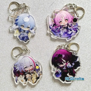 Op de afbeelding: Vier kleurrijke anime-personage sleutelhangers met zilveren sleutelringen. Elke sleutelhanger heeft een ander personage met een uniek ontwerp en levendige kleuren.