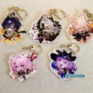 Op de afbeelding: Vijf kleurrijke anime-personage sleutelhangers met zilveren sleutelringen. Elke sleutelhanger heeft een ander personage met een uniek ontwerp en kleurenschema. De personages zijn afgebeeld in een chibi-stijl, met grote hoofden en kleine lichamen. De sleutelhangers zijn gemaakt van helder acryl en hebben een glanzende afwerking.