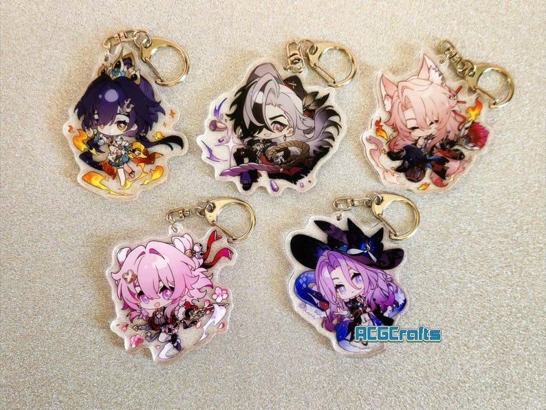 Op de afbeelding: Vijf kleurrijke anime-personage sleutelhangers met zilveren sleutelringen. Elke sleutelhanger heeft een ander personage met een uniek ontwerp en kleurenschema. De personages zijn afgebeeld in een chibi-stijl, met grote hoofden en kleine lichamen. De sleutelhangers zijn gemaakt van helder acryl en hebben een glanzende afwerking.