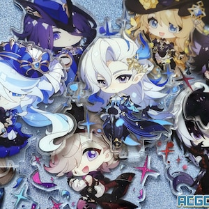 May include: A collection of eight anime-style character acrylic charms. The charms are all different characters with various colors and designs. The characters are all in a chibi style, with large heads and small bodies. The charms are all on a sparkly blue background.