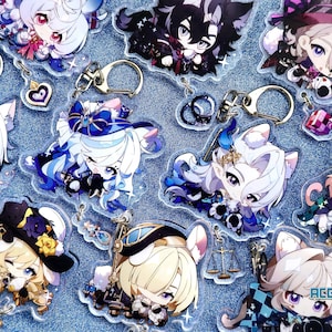 May include: A collection of colorful anime character keychains with glitter accents. The keychains feature characters with white, black, and blue hair, wearing various outfits. Some keychains have cat ears and tails. The keychains are on a blue glitter background.