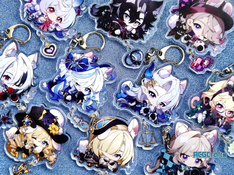 May include: A collection of colorful anime character keychains with glitter accents. The keychains feature characters with white, black, and blue hair, wearing various outfits. Some keychains have cat ears and tails. The keychains are on a blue glitter background.