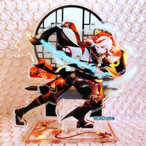 Peut inclure: Un support en acrylique transparent avec un personnage d'anime coloré tenant une épée. Le personnage porte une tenue rouge et noire avec une ceinture blanche et dorée. Le support a une base rouge avec un motif doré. Le personnage se tient devant une fenêtre de style japonais.