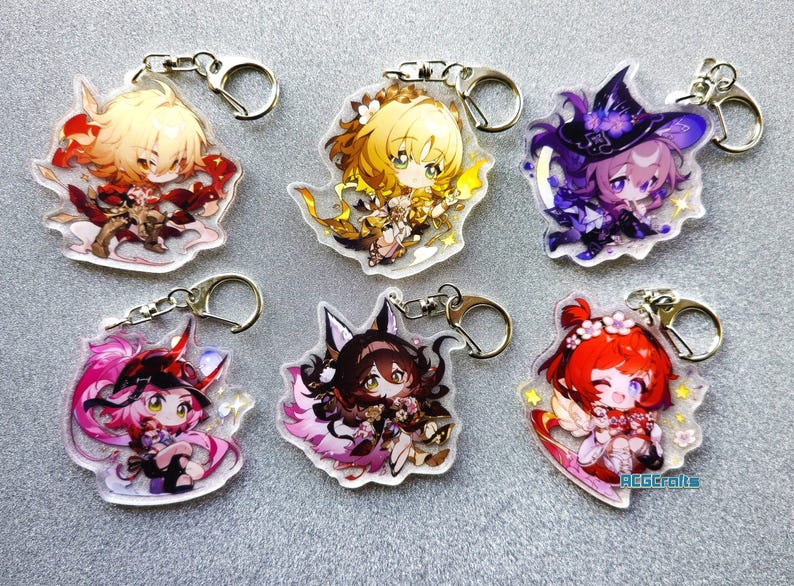 Op de afbeelding: Zes kleurrijke anime-personage sleutelhangers met zilveren sleutelringen. Elke sleutelhanger heeft een ander personage met een uniek ontwerp en kleurenschema. De personages zijn afgebeeld in chibi-stijl, met grote hoofden en kleine lichamen.