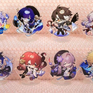 May include: Set of ten anime character acrylic charms. The charms feature various characters with different coloured hair and clothing. The characters are all smiling and have large eyes. The charms are attached to clear acrylic stands.