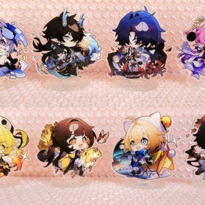 May include: Set of ten anime character acrylic charms. The charms feature various characters with different coloured hair and clothing. The charms are all in a cartoon style and have a glossy finish.