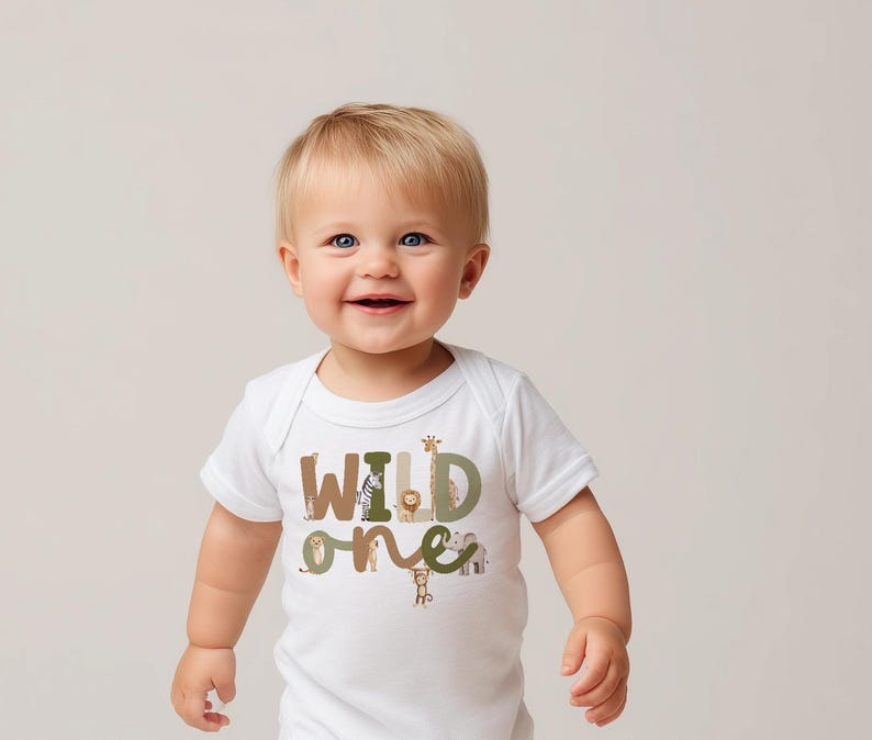 May include: A white baby bodysuit featuring the text "WILD ONE" in brown, green, and tan. The letters are adorned with animal illustrations, such as a giraffe, lion, and monkey. The baby is smiling.