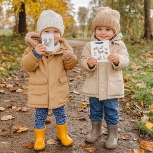 May include: Two children in tan jackets and knit hats hold cards with animal illustrations. One card shows a squirrel, the other displays the word "Wildlife" above various animal drawings. They wear blue pants and yellow and gray boots, standing on a path with fallen leaves.