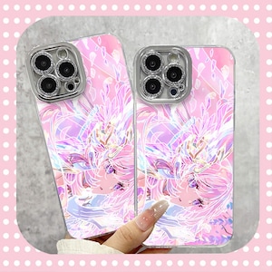 May include: Two phone cases with a pink and purple anime-style design. The cases have a clear border and a silver camera lens protector. The design features a character with pink hair and a floral background.