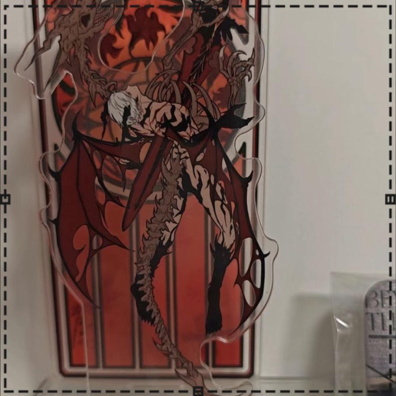 May include: A clear acrylic stand featuring a detailed illustration of a winged demon with red wings and a muscular physique. The artwork has a dark, gothic theme with a red and black color palette.