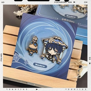以下が含まれることがあります： キャラクターデザインの2つのエナメルピン。1つのピンは、青と金のアクセントが付いたボトル型のオブジェクトを描いています。もう1つのピンは、青い髪と帽子を持つキャラクターを示しています。ピンは「Wanderer」という単語が付いた青い背景にあります。