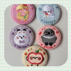 May include: Embroidered circular patches with adorable animal designs: a chick, bunny, bird, and apple. Each patch has a name embroidered on it: Rafayel, Zayne, Xavier, Sylus, and an apple character. The patches are in pastel shades.
