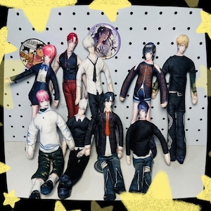May include: A collection of handmade anime-style dolls, each with unique outfits and hairstyles. The dolls are arranged on a dotted background, with two circular pinback buttons. The dolls are in various poses.
