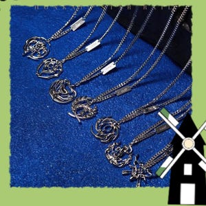 May include: Several silver necklaces with different pendant designs, such as abstract shapes and circular patterns. The necklaces are presented on a textured blue surface, highlighting their intricate details and chain styles.