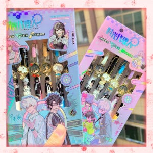 Può includere: Due scatole di penne con disegni di personaggi in stile anime. Le scatole sono in colori pastello con testo e illustrazioni giapponesi. Ogni penna ha un ciondolo decorativo. Le penne sono nere, blu e rosa.