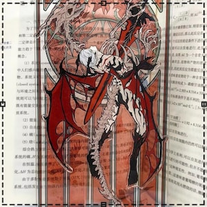 May include: A clear acrylic standee featuring a detailed illustration of a winged demon with red and black accents. The artwork depicts a figure with white hair and a skeletal design, set against a backdrop of text and a stained-glass-like pattern.