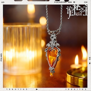 May include: A silver-toned pendant necklace with an amber-colored, teardrop-shaped gemstone. The pendant has ornate filigree detailing. The background includes lit candles and the text "Lord of Mysteries".