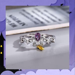 May include: A silver adjustable ring with a pear-shaped purple gemstone. The ring features a bow and leaf design with small clear stones. A unique piece of jewellery.