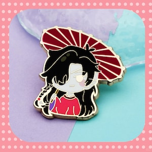 May include: An enamel pin depicting a cartoon character with black hair, a red shirt, and a red parasol. The pin has a gold outline and a light blue background.