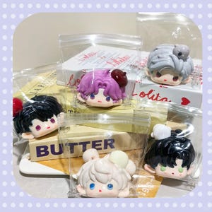 May include: Several small, colorful character figurines in clear plastic bags. The figurines have different hair colors and accessories, and are placed on top of butter packages. The word "BUTTER" is visible on one package.