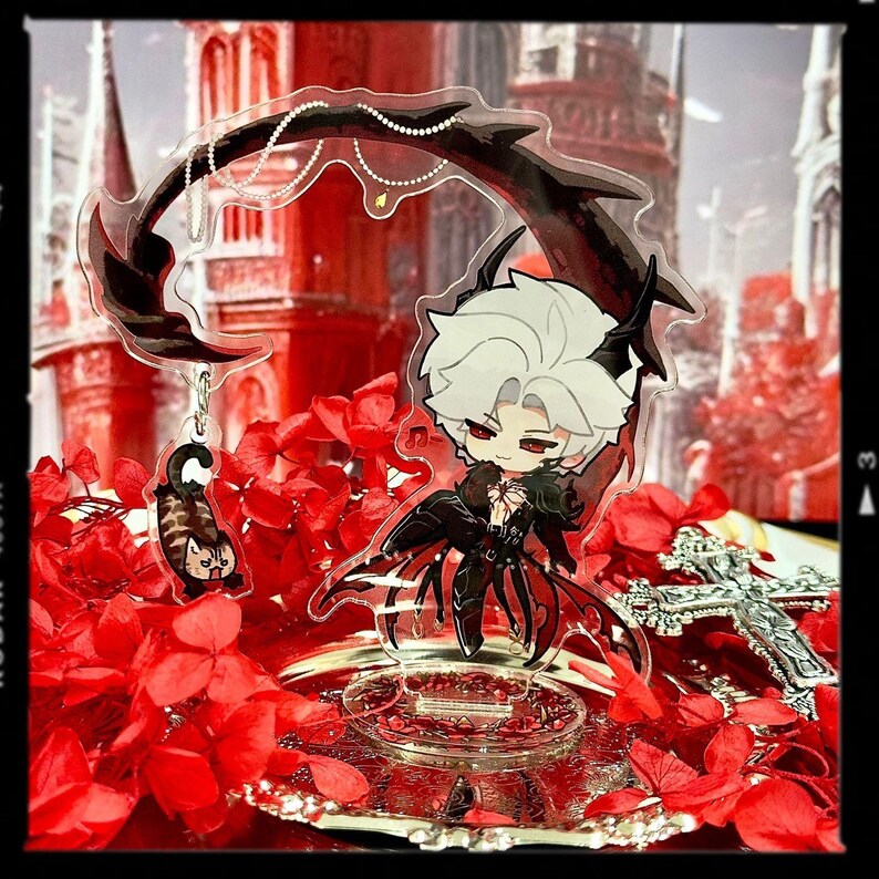 May include: A clear acrylic charm featuring a chibi anime character with white hair, red eyes, and a black outfit. The charm has a decorative black element and a small cat charm. The background is a red floral arrangement.