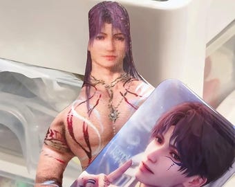 May include: A printed cutout of a person with purple hair and intricate body art, holding a rectangular card with a male anime character. The card has the text "Temple Isura" and a blue sky background.