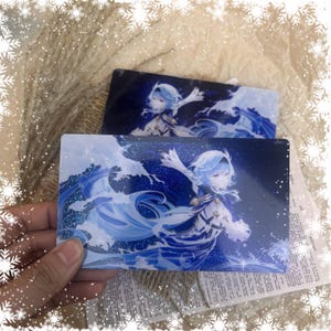May include: Two rectangular cards featuring a character with light blue hair and a flowing outfit, set against a backdrop of stylized ocean waves. The cards have a dark blue background with sparkling accents, creating a dynamic and artistic design.