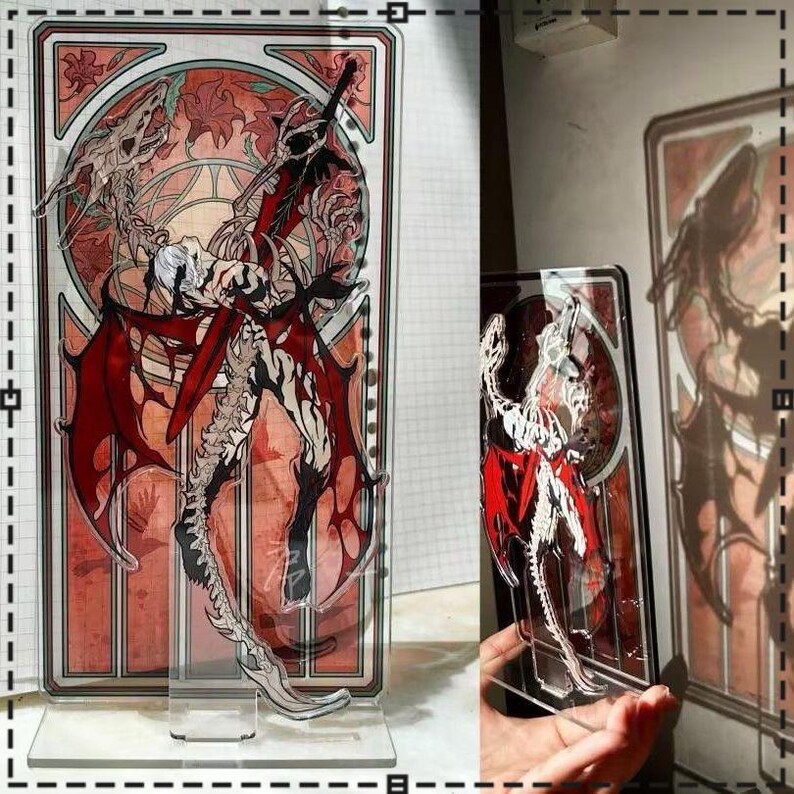 May include: A clear acrylic stand featuring a detailed illustration of a winged figure with a sword, set against a stained-glass style background. The artwork incorporates red, white, and black colors, with a decorative base.