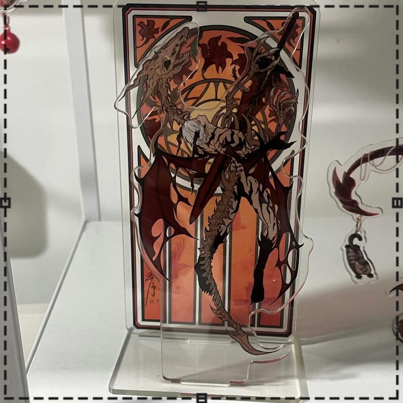 May include: A clear acrylic stand featuring a detailed illustration of a winged figure with a sword, set against an orange and brown stained-glass style background. The artwork has a fantasy theme, with intricate details and a dynamic pose.