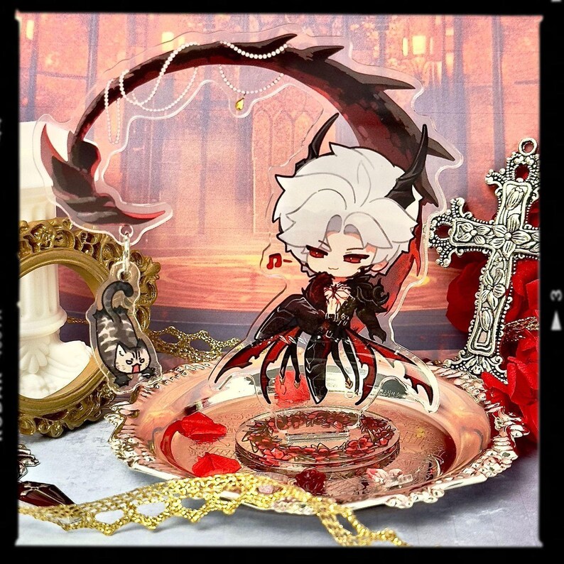 May include: A decorative acrylic figure of a character with white hair and red eyes, wearing a black and red outfit. The figure is on a silver tray with red rose petals. A matching keychain of a cat is also present.
