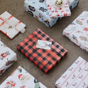 May include: A collection of wrapped gifts with various festive patterns. The gifts are wrapped in paper with designs featuring dogs, cats, reindeer, and other holiday motifs. Some of the gifts are tied with twine and have gift tags attached.