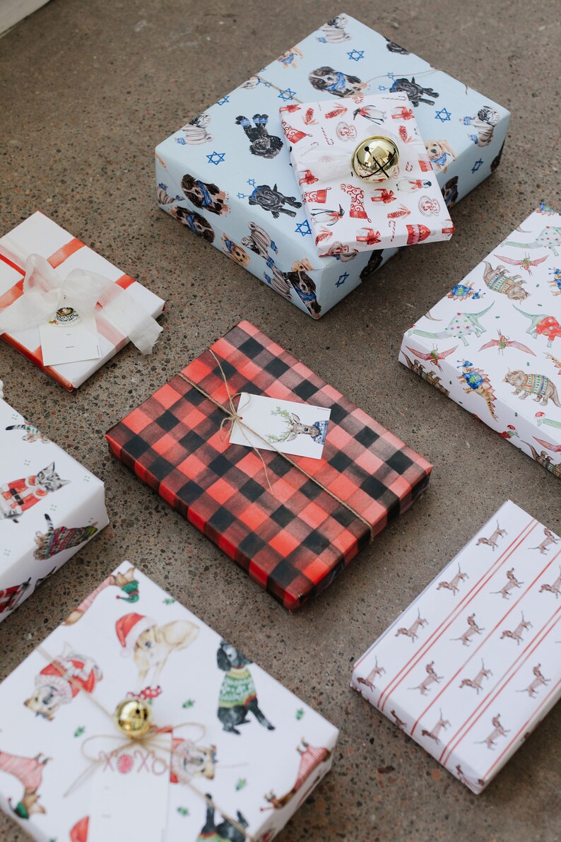 May include: A collection of wrapped gifts with various festive patterns. The gifts are wrapped in paper with designs featuring dogs, cats, reindeer, and other holiday motifs. Some of the gifts are tied with twine and have gift tags attached.