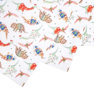 May include: White wrapping paper with a repeating pattern of dinosaurs wearing Christmas sweaters and hats. The dinosaurs are in various colors, including red, green, blue, and brown.