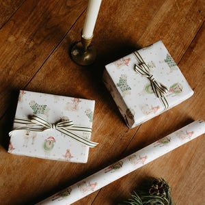 May include: Two wrapped presents with a sheep pattern, tied with striped ribbon, are on a wooden surface. A roll of matching wrapping paper and a lit candle in a brass holder are also present, suggesting a festive occasion.