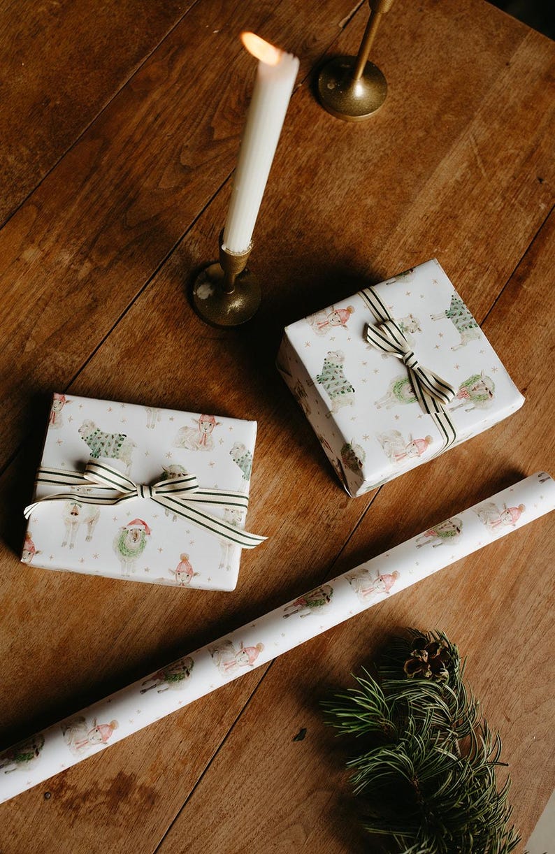 May include: Two wrapped presents with a sheep pattern, tied with striped ribbon, are on a wooden surface. A roll of matching wrapping paper and a lit candle in a brass holder are also present, suggesting a festive occasion.