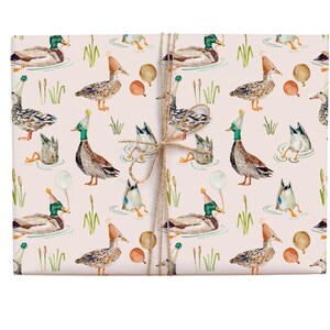 May include: Pink wrapping paper with a repeating pattern of ducks wearing party hats and holding balloons. The ducks are in various poses, some swimming, some standing, and some flying. The background is a light pink colour.