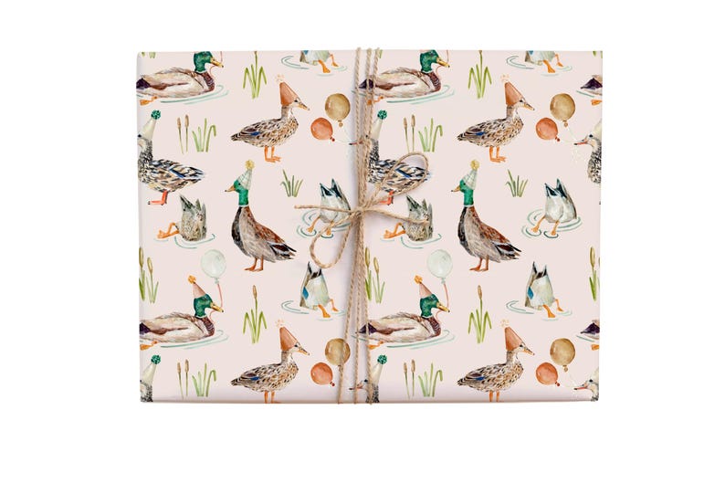 May include: Pink wrapping paper with a repeating pattern of ducks wearing party hats and holding balloons. The ducks are in various poses, some swimming, some standing, and some flying. The background is a light pink colour.