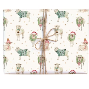 May include: Wrapped gift with a festive sheep pattern. The design features watercolour illustrations of sheep wearing sweaters, Santa hats, and wreaths, with gold stars on a cream background. Tied with twine.