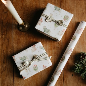 May include: Two wrapped gifts with striped bows and a roll of matching wrapping paper featuring a festive llama design. A lit candle and pine sprig with a pinecone are on a wooden surface.
