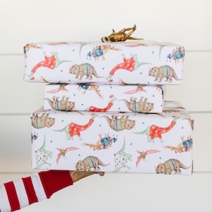 May include: Three wrapped gifts with a dinosaur pattern. The wrapping paper is white with red, blue, and green dinosaurs wearing sweaters. The gifts are stacked on top of each other.