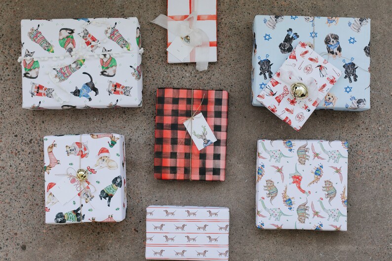 May include: Assortment of eight gift wrap designs featuring various animal patterns. The designs include cats wearing sweaters, dogs wearing sweaters, dachshunds, dinosaurs, and a plaid pattern.