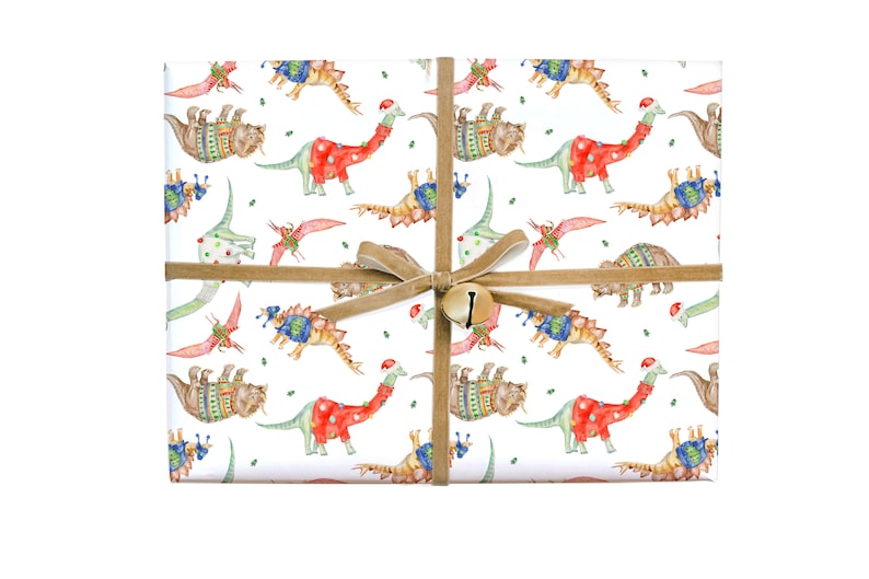 May include: White wrapping paper with a repeating pattern of dinosaurs wearing Christmas sweaters and hats. The dinosaurs are in shades of green, blue, red, and brown. The paper is tied with a brown ribbon and a gold bell.