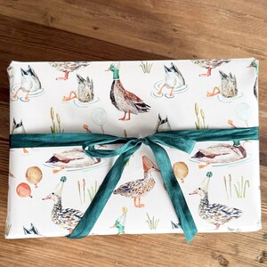 May include: White gift wrap featuring a pattern of ducks wearing party hats and holding balloons. The wrap is tied with a green ribbon.